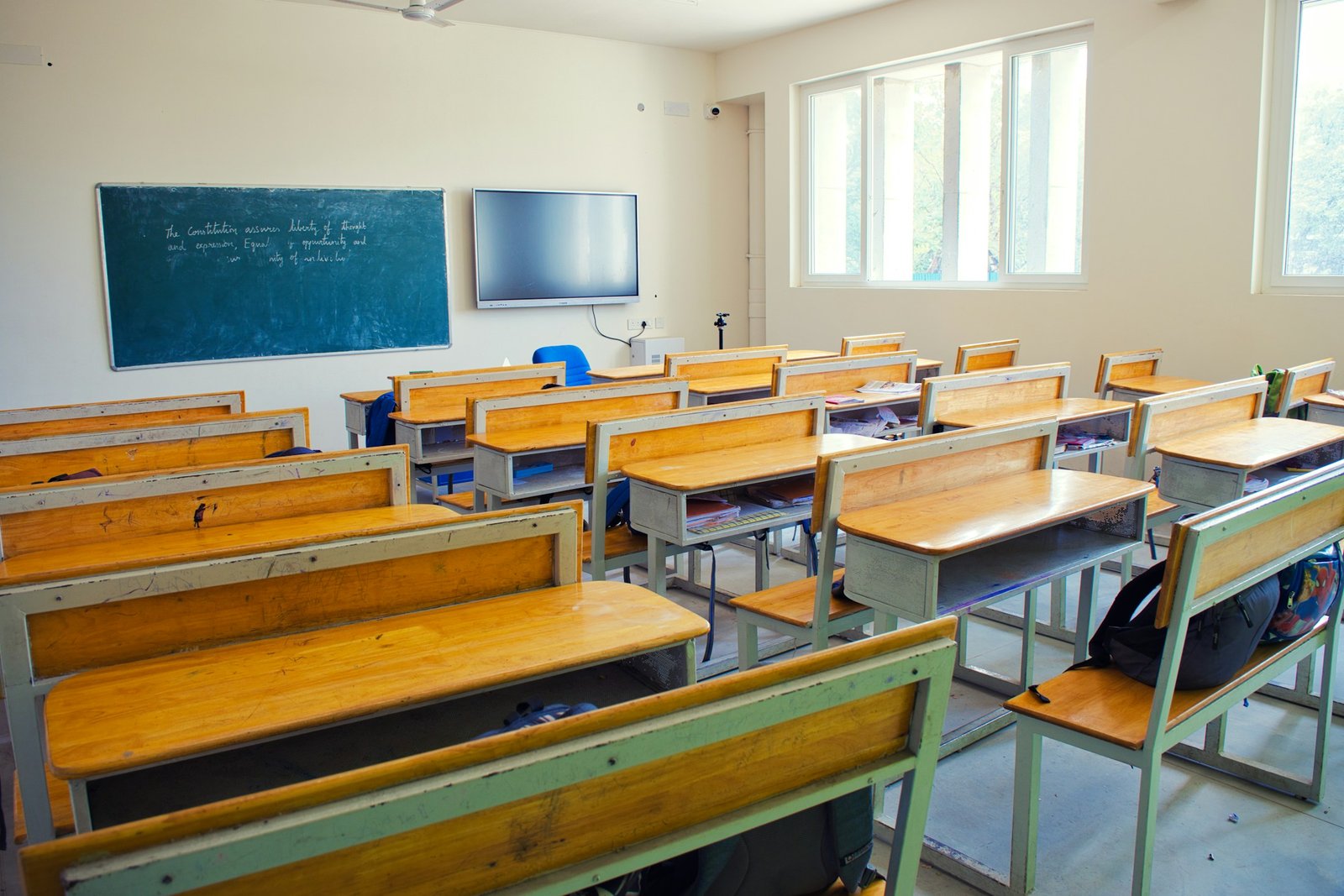 A bright classroom in Chennai with rows of wooden desks and a chalkboard